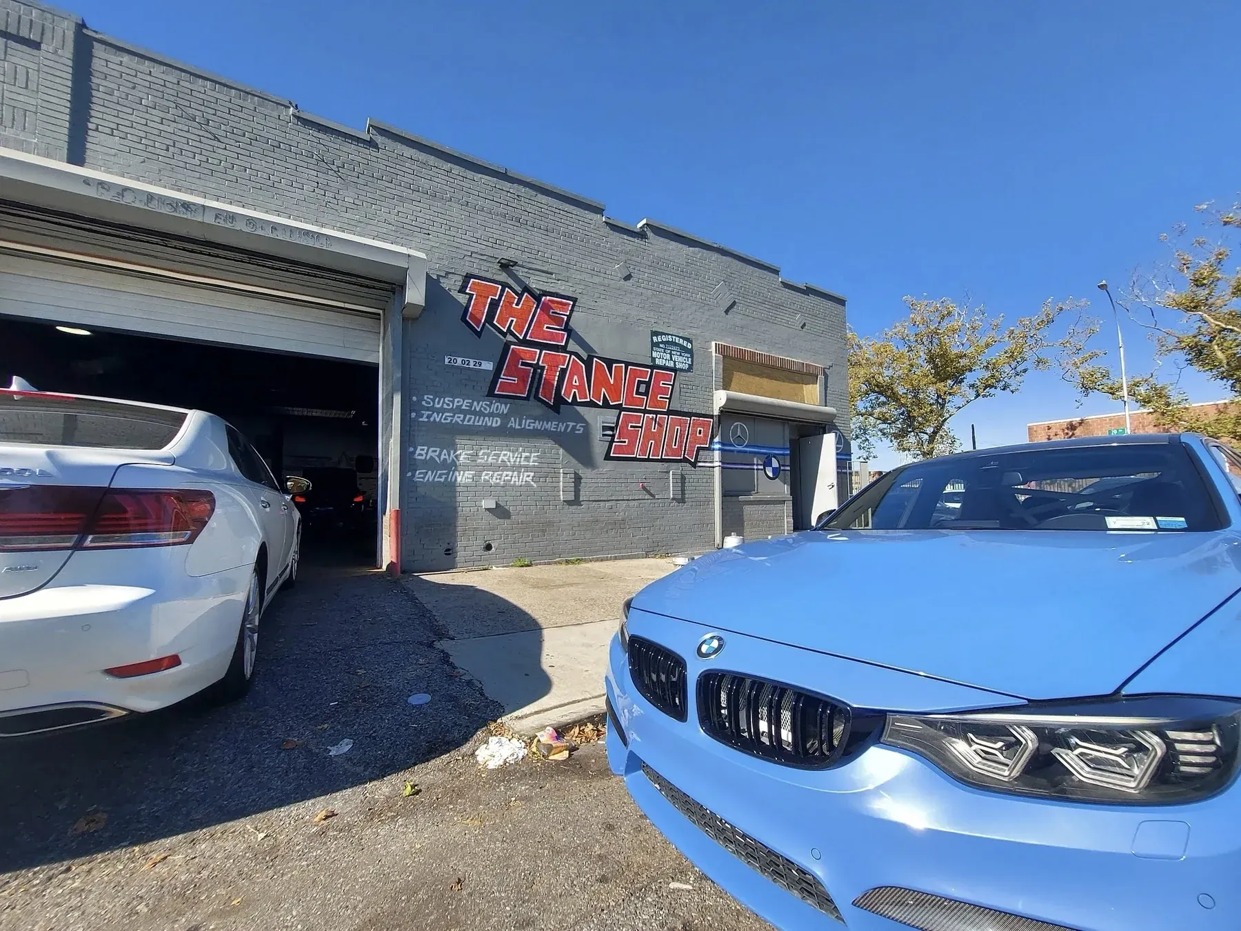 A blue BMW M parked outside The Stance Shop beneath its painted sign