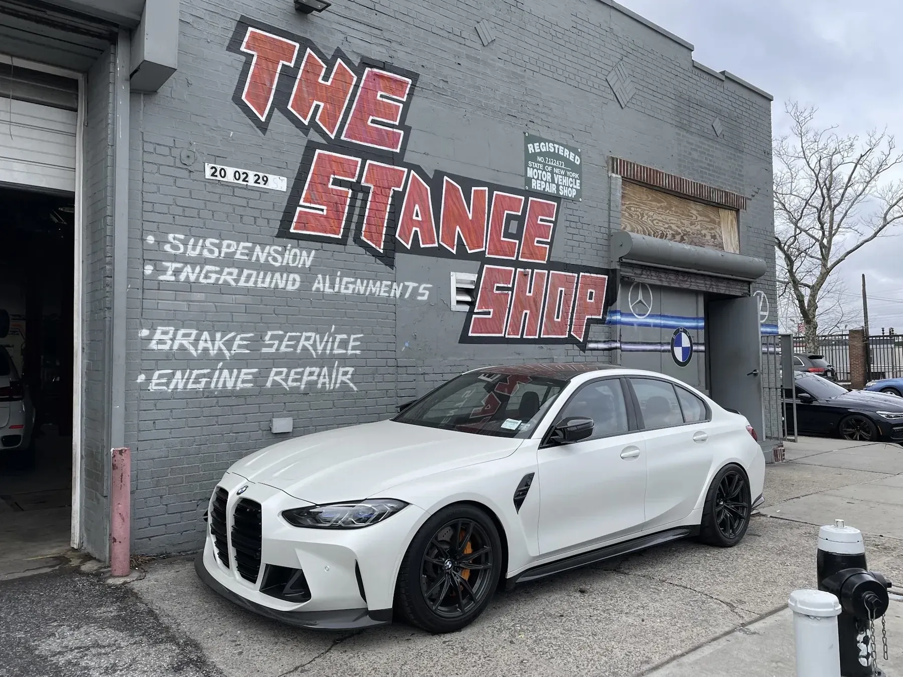 A white BMW M3 outside The Stance Shop, beneath the shop's hand-painted sign on 29th Street